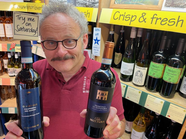 Photograph shows Duncan holding Saturday's Free Tasting wines: white wine is Falanghina and red wine is Primitivo.