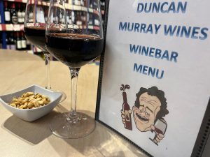 Image shows wine bar menu, 2 wine glasses and a bowl of nuts