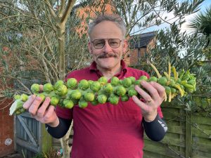 Image shows Duncan Murray holding a stalk of brussels sprouts